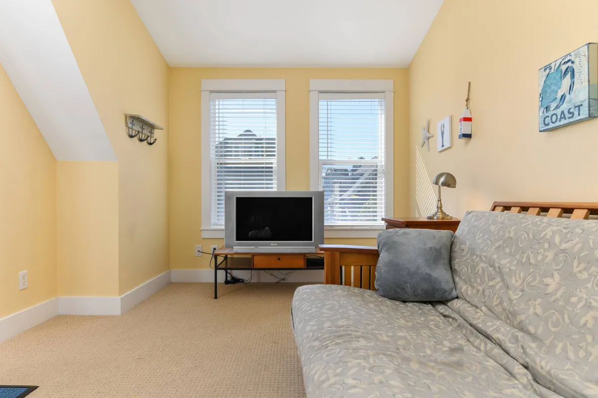 A light-filled living room with a comfortable sofa, a television, and large windows that let in natural light. Tasteful decorative items and soft colors create a welcoming, relaxed environment ideal for socializing or quiet moments.