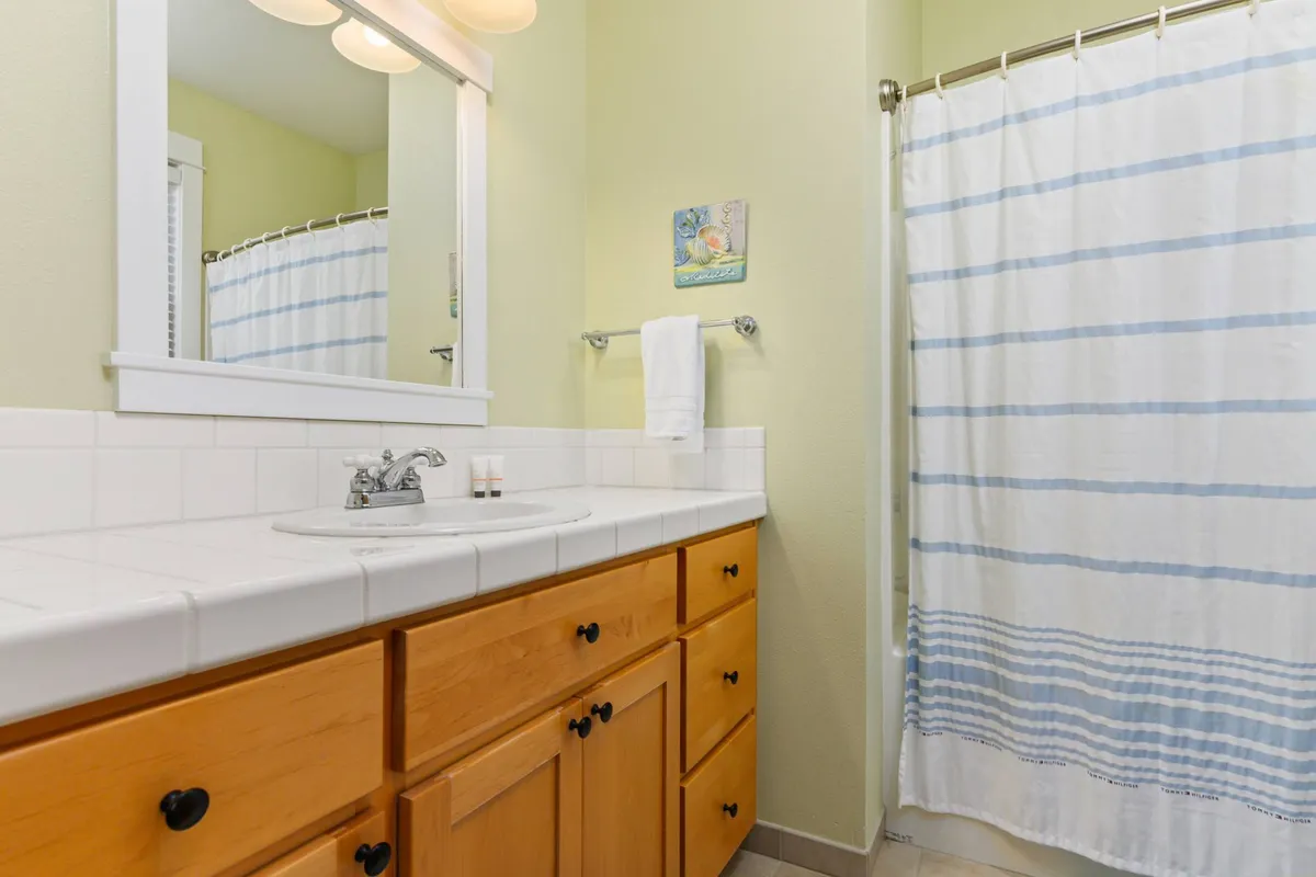 A bright, modern bathroom with a vanity sink, mirror, and wooden cabinetry. The soft lighting and clean design create a soothing space for morning and evening routines, highlighting the convenience of the shared guest bathroom.