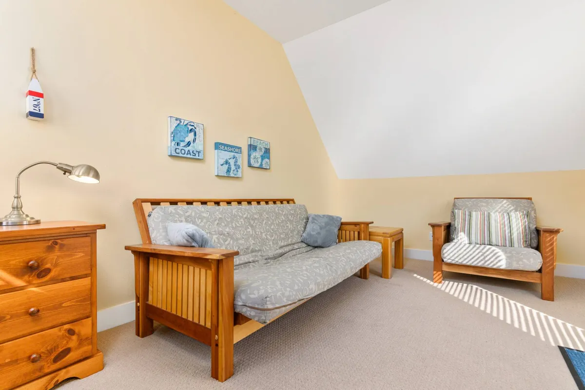 A detached bonus living space furnished with a futon sofa, striped chair, and artistic wall decor. The cozy, flexible layout makes it suitable for both sleeping and lounging, providing a quiet retreat away from the main house.