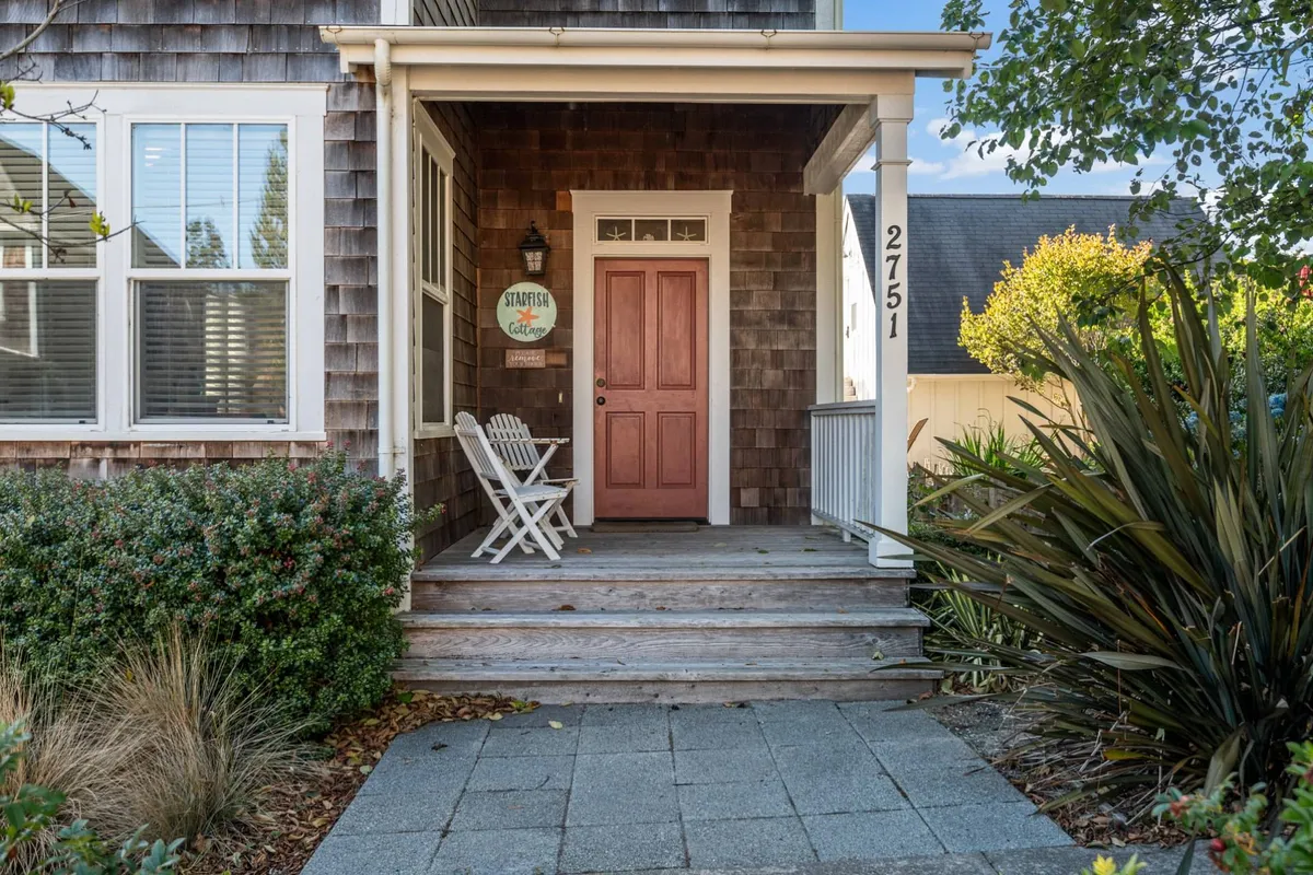The inviting exterior of Starfish Cottage, featuring a charming sign with the cottage’s name, a cozy front porch with white chairs, and well-kept landscaping. The scene exudes a warm, welcoming atmosphere perfect for arriving guests and their pets.