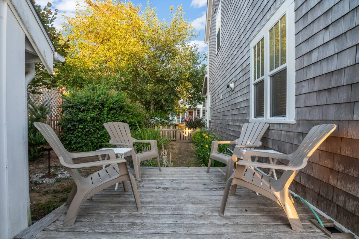 A wooden deck bordered by a fence, featuring Adirondack chairs for lounging and surrounded by vibrant greenery—an inviting outdoor space perfect for relaxing, playing, or spending time with pets and kids.