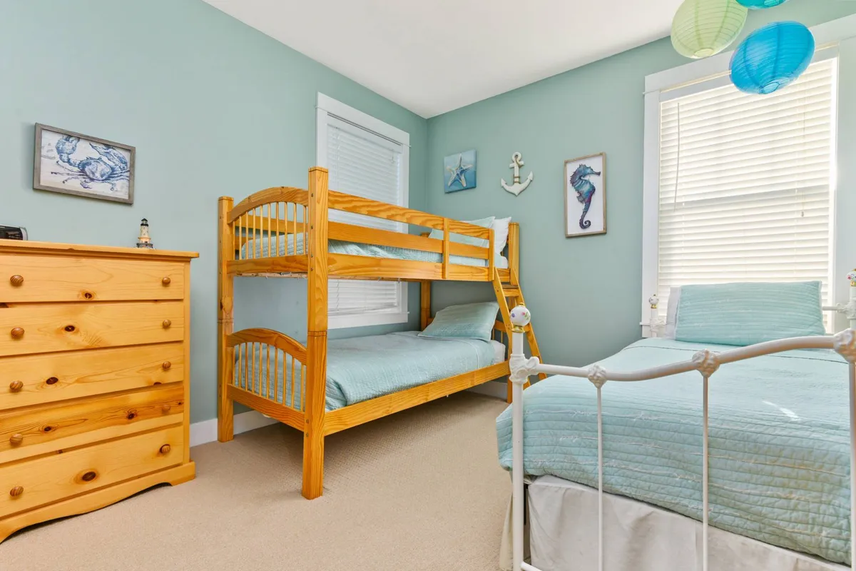 A playful and inviting children’s room featuring a twin-over-twin bunk bed, a single bed, and cheerful nautical-themed decor. Colorful lanterns and wall art create a fun, family-friendly environment perfect for children to relax, play, or read before bedtime.