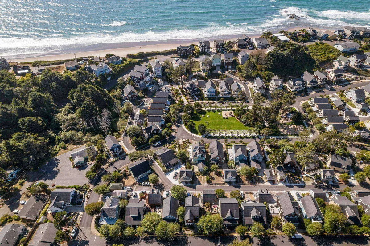 A sweeping view that showcases the beachfront, a lush green park area, and the neighborhood's inviting layout. Ocean waves roll onto the shore, while families and visitors can be seen enjoying the open park spaces and the nearby beach. The image conveys a sense of community, outdoor activity, and the natural beauty of the Lincoln City coastline.