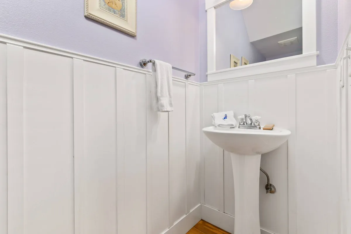 A small, inviting half bath with a pedestal sink, towel rack, framed artwork, and mirror. It's a bright and efficient space that offers convenience just off the main living and dining areas.